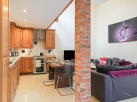 A kitchen with wooden cabinets and a dining table set with cups and plates next to a living area with sofas and a brick pillar at Cob Barn in Aylesbeare