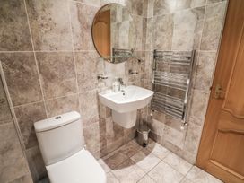 A bathroom with a toilet sink round mirror heated towel rack and a wooden door at Cob Barn in Aylesbeare