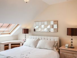 A bedroom with a white bedspread two bedside tables with lamps a mirror on the wall and a skylight window at Cob Barn in Aylesbeare