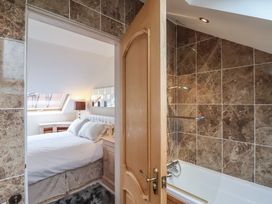 A bedroom with a bed and lamp seen through an open door next to a bathroom with a bathtub and tiled walls at Cob Barn in Aylesbeare