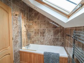 A bathroom with a bathtub under a skylight window and brown tiled walls at Cob Barn in Aylesbeare