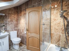 A bathroom with a toilet a sink with cabinet a wooden door and a bathtub with shower at Cob Barn in Aylesbeare