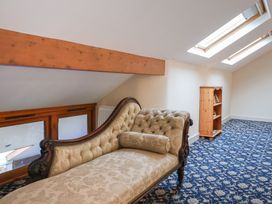 A room with a patterned carpet a wooden bookshelf and a vintage upholstered chaise longue under skylight windows at Cob Barn in Aylesbeare