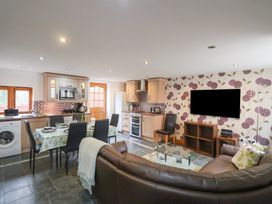 An open-plan kitchen and living room with a dining table set and a leather sofa at Ivy Cottage in Aylesbeare