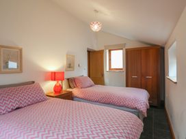 A bedroom with two single beds with pink chevron bedding a wooden wardrobe and a red lamp at Ivy Cottage in Aylesbeare
