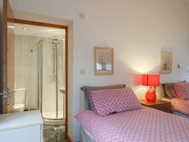 A bedroom with two beds with pink chevron patterned bedding a red lamp on a bedside table and a bathroom with a shower visible through an open door at Ivy Cottage in Aylesbeare