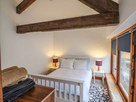 A bedroom with a white bed and bedside tables with lamps under wooden ceiling beams at Ivy Cottage in Aylesbeare