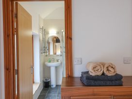 A bathroom with a wooden door a white sink and mirror and folded towels on a wooden dresser at Ivy Cottage in Aylesbeare