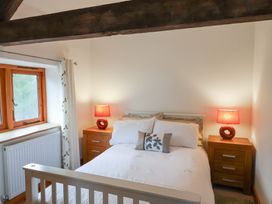 A bedroom with a white bed between two wooden nightstands with red lamps and a window at Ivy Cottage in Aylesbeare