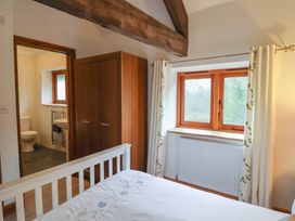 A bedroom with a wooden wardrobe a window with curtains and an en suite bathroom at Ivy Cottage in Aylesbeare
