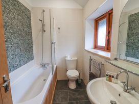 A bathroom with a bathtub shower combination a toilet a sink with toiletries and a window at Ivy Cottage in Aylesbeare