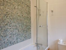 A bathroom with a bathtub shower combination and pebble tiled wall at Ivy Cottage in Aylesbeare