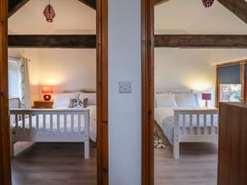 Two bedrooms each with a white bed a nightstand with a lamp and wooden beams on the ceiling at Ivy Cottage in Aylesbeare
