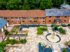 An outdoor courtyard with a tiled fountain in the center surrounded by planters and brick buildings with red doors and windows at Ivy Cottage in Aylesbeare