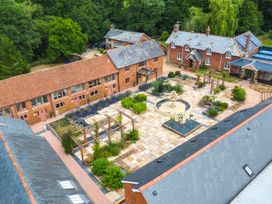 An aerial view of a courtyard with a stone fountain surrounded by garden beds and red brick buildings with tiled roofs at Ivy Cottage in Aylesbeare