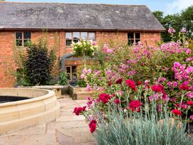 A stone patio with flowers and plants in front of a brick house at Ivy Cottage in Aylesbeare