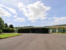 An outdoor area with grass, trees, clouds and caravans at Stable Cottage Cottonshopeburnfoot near Otterburn