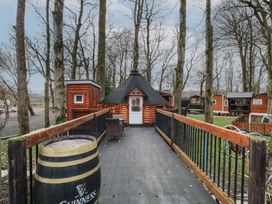 A wooden hut with a conical roof at the end of a wooden walkway with railings surrounded by trees at Hexagon Hut - Dec Update in Dungiven Londonderry