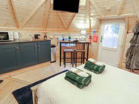 A small wooden room with a bed, green towels, a kitchenette with microwave and kettle, a high table with stools, and a door with a window at Hexagon Hut - Dec Update in Dungiven Londonderry