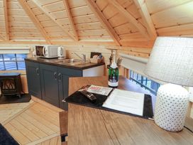 A wooden kitchen area with a microwave oven sink and a black stove next to a table with a lamp bottle and documents at Hexagon Hut - Dec Update in Dungiven Londonderry