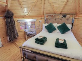 A bedroom with a bed with green pillows and towels a lamp on a mirrored nightstand and coats hanging on the wall at Hexagon Hut - Dec Update in Dungiven Londonderry