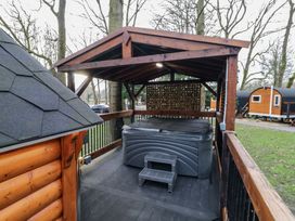 An outdoor covered hot tub on a wooden deck with trees and small cabins in the background at Hexagon Hut - Dec Update in Dungiven Londonderry