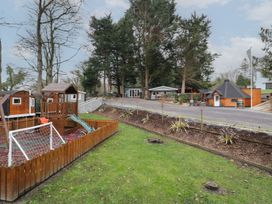An outdoor area with a fenced wooden playground and slide and several small wooden buildings and trees at Hexagon Hut - Dec Update in Dungiven Londonderry