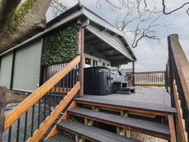 A raised wooden deck with stairs leading up to a covered area with a hot tub and outdoor seating surrounded by trees at Mill View in Dungiven Londonderry