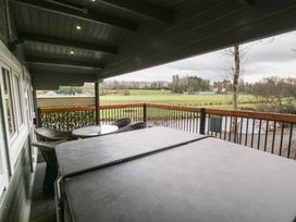 A covered balcony with a hot tub and a table with chairs overlooking a grassy field at Mill View in Dungiven Londonderry