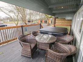 A covered outdoor deck with a round glass table and wicker chairs next to a hot tub overlooking a parking area and trees at Mill View in Dungiven Londonderry
