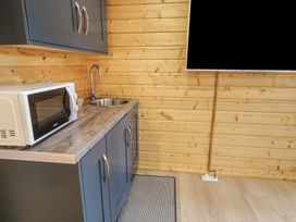 A kitchenette with blue cabinets a microwave a sink a wall-mounted TV and wooden wall panels at Mill View in Dungiven Londonderry