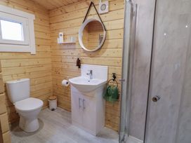 A bathroom with a toilet sink shower wooden walls and a round mirror at Mill View in Dungiven Londonderry
