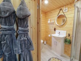 A bathroom with wooden walls featuring a white sink cabinet mirror shower and two grey bathrobes hanging at Mill View in Dungiven Londonderry