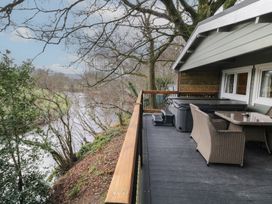 An outdoor deck with wicker chairs, a glass table and a hot tub overlooking a river and trees at Mill View in Dungiven Londonderry