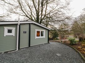 An exterior view of a single story house with green paneling and white window frames on a gravel driveway with trees and plants around at The Old Priory in Dungiven Londonderry
