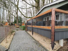 A gravel pathway next to a raised porch with wooden railing surrounded by trees and small wooden cabins at Mill View in Dungiven Londonderry