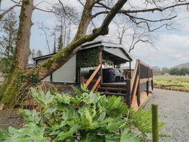 An exterior view of a small house with a covered porch and wooden railing surrounded by large trees and greenery at Mill View in Dungiven Londonderry