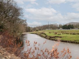 A river flowing alongside grass and trees with a bench on the grass at Mill View in Dungiven Londonderry