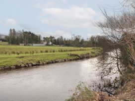 A river flowing beside green fields with trees and farm buildings in the distance at Mill View in Dungiven Londonderry