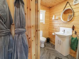 A bathroom with wooden walls a toilet a white sink with cabinet a round mirror a green towel and two gray bathrobes at Owenbeg Dungiven Londonderry