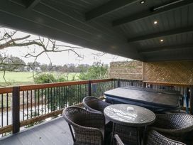 A covered balcony with a hot tub and wicker chairs around a glass table overlooking a field at Owenbeg in Dungiven Londonderry