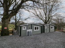 A green cabin with white trim surrounded by large trees and gravel ground at Owenbeg in Dungiven Londonderry