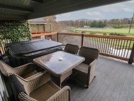 An outdoor covered patio with a hot tub a glass table and four wicker chairs overlooking a grassy field and trees at The Roe in Dungiven Londonderry
