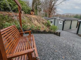 A wooden garden swing on a gravel area with a grey building and trees in the background at The Roe in Dungiven Londonderry
