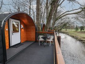 A wooden pod with white door on a deck with table and two chairs beside a river at Hazel in Dungiven Londonderry