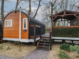 A small cabin with wooden siding and black roof next to a covered wooden deck surrounded by trees at Hazel in Dungiven Londonderry