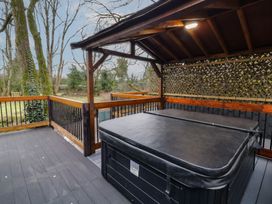 A covered deck with a hot tub and wooden railing overlooking trees at Hazel in Dungiven Londonderry