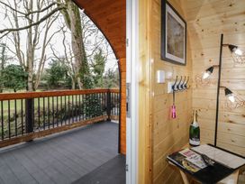 A wooden balcony with railing overlooking trees and a grassy area next to an interior space with wooden walls a small table with a bottle and remote and a floor lamp Hazel Dungiven Londonderry