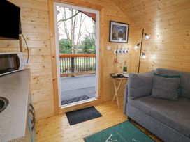 Interior view of a wooden cabin with a gray sofa a side table with a bottle and a lamp and an open door leading to a deck at Hazel in Dungiven Londonderry