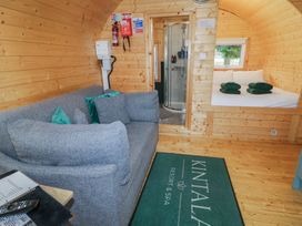 A wooden pod interior with a grey sofa and pillows a small bed with towels on it and a shower cubicle at Hazel in Dungiven Londonderry